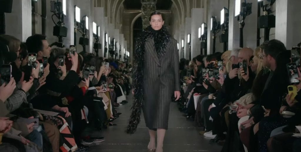 Female model walking down runway at the Tory Burch F/W 2024 show at NYFW, dressed in tinsel scarf and tailored suit coat.